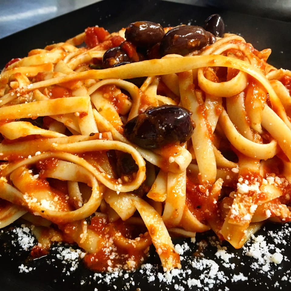 Sauce's pasta dish with thick noodles, red sauce, black olives, and grated cheese.