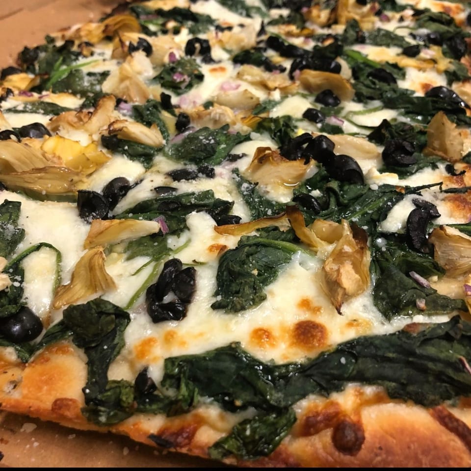 Close-up of a Sauce pizza with melted cheese, spinach, black olives, and artichoke hearts.