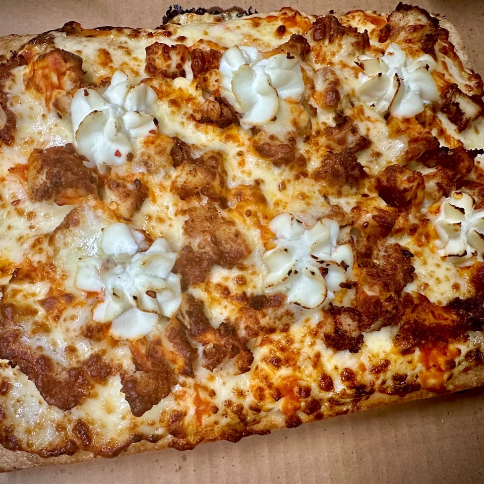 Close-up of a Sauce pizza with melted cheese, crispy chicken, and dollops of white sauce.