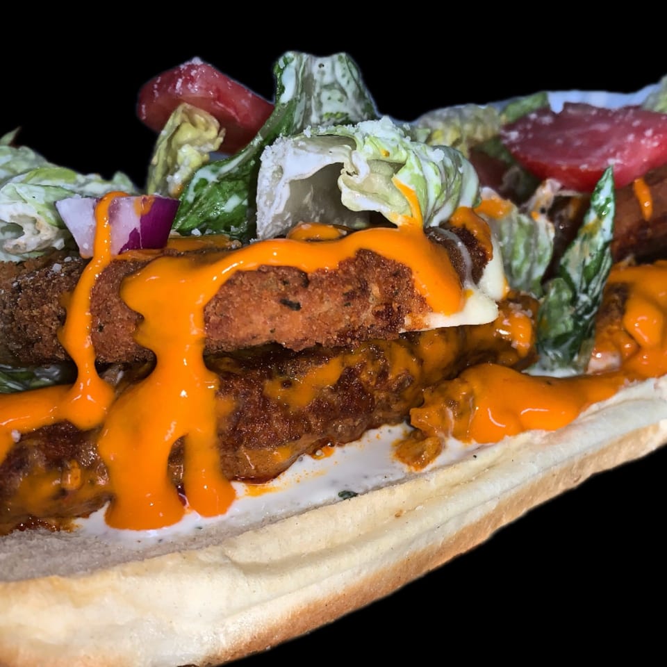 Close-up of a sub sandwich with crispy fried chicken, orange sauce, lettuce, tomatoes, and red onions.
