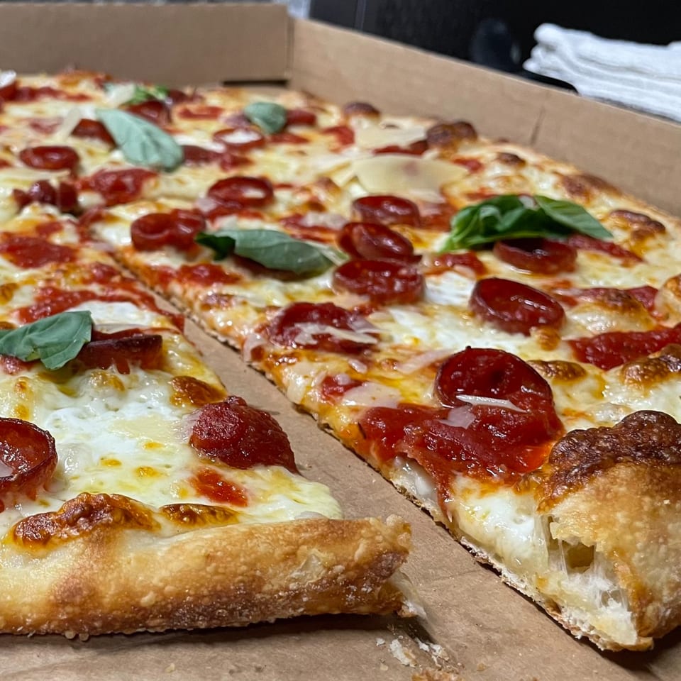A Sauce pizza with pepperoni, melted mozzarella, and fresh basil leaves in a cardboard box.