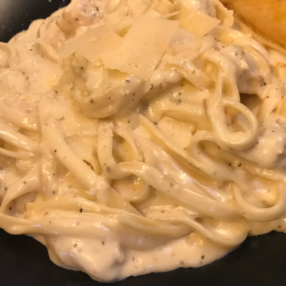 Creamy fettuccine alfredo with shaved Parmesan cheese and black pepper on a dark plate.