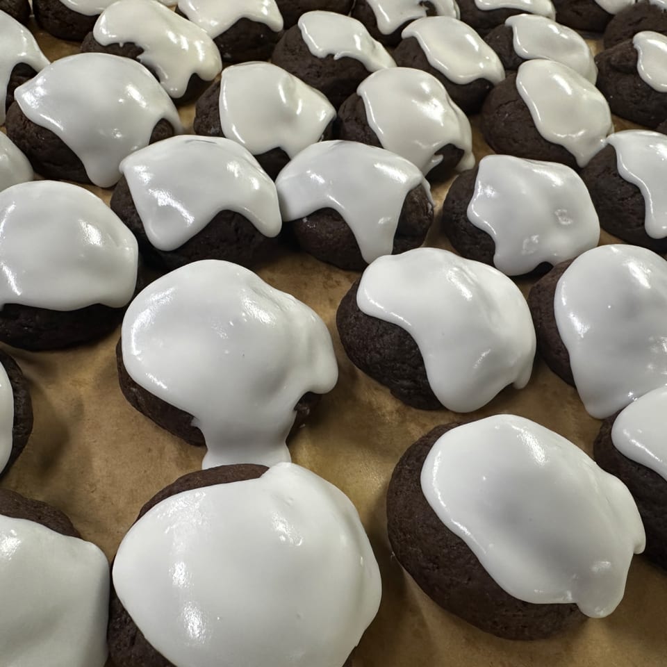 Rows of dark chocolate cookies with white icing on a brown surface.
