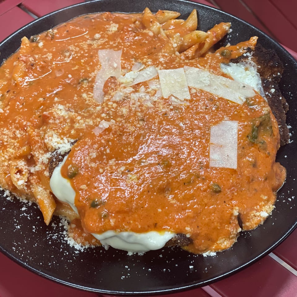 Penne pasta with rich red sauce, melted white cheese, and grated Parmesan on a black plate.