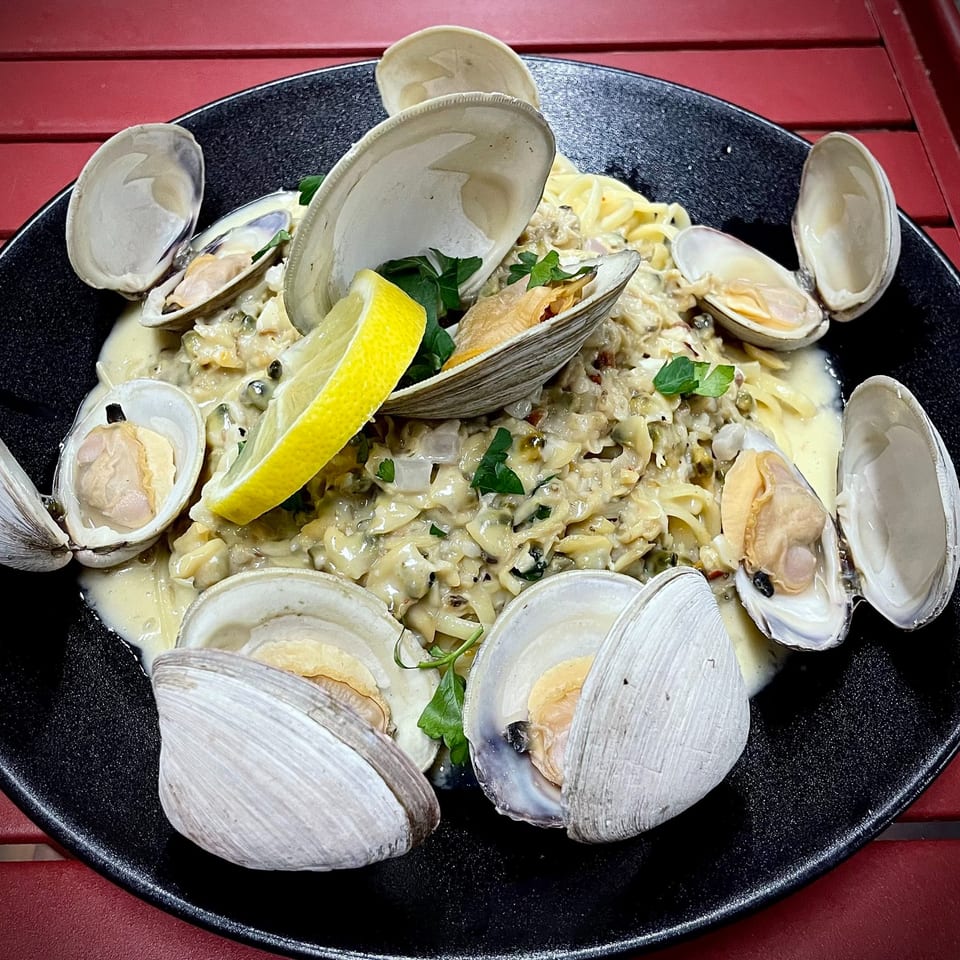 Clams in a creamy sauce with pasta, garnished with parsley and lemon, on a black plate.