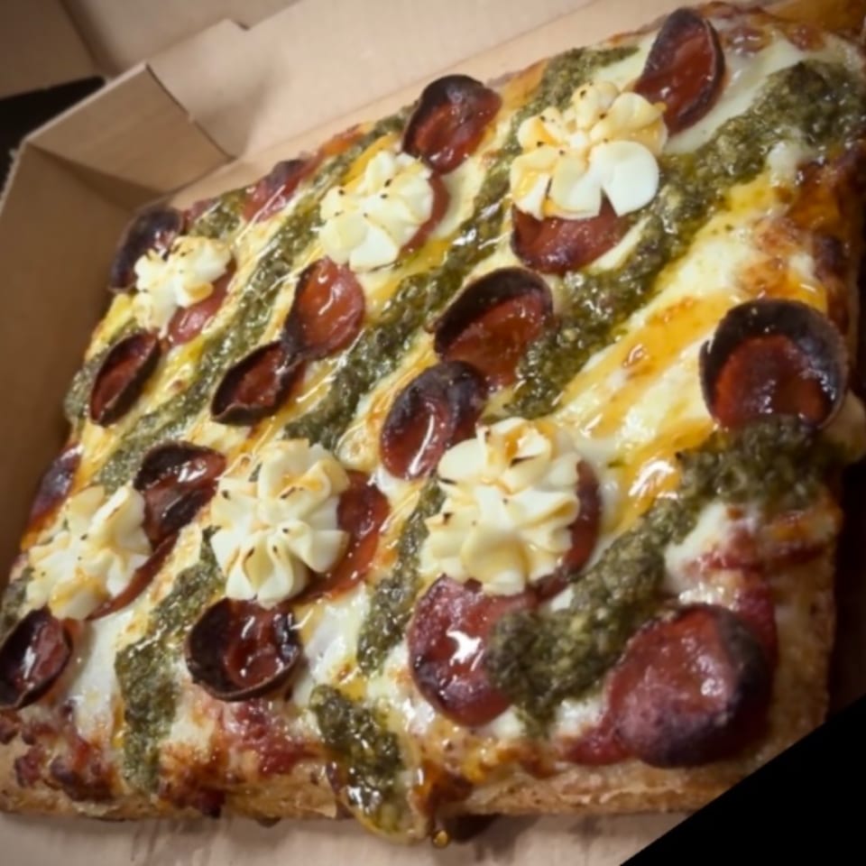 A square pizza from Sauce, topped with pepperoni, pesto, and dollops of white cheese.