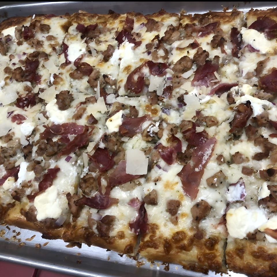 Close-up of a rectangular pizza with white cheese, sausage, and prosciutto on a metal tray.