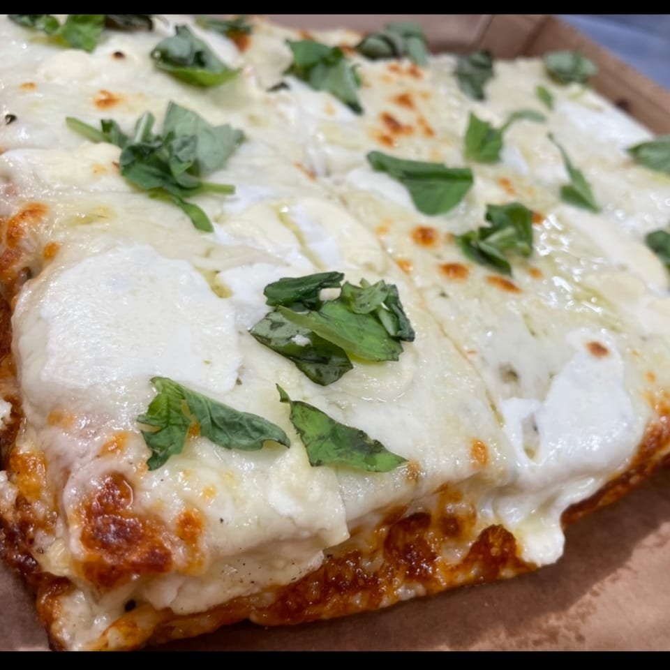 Close-up of a rectangular white pizza from Sauce, topped with melted cheese and fresh basil.