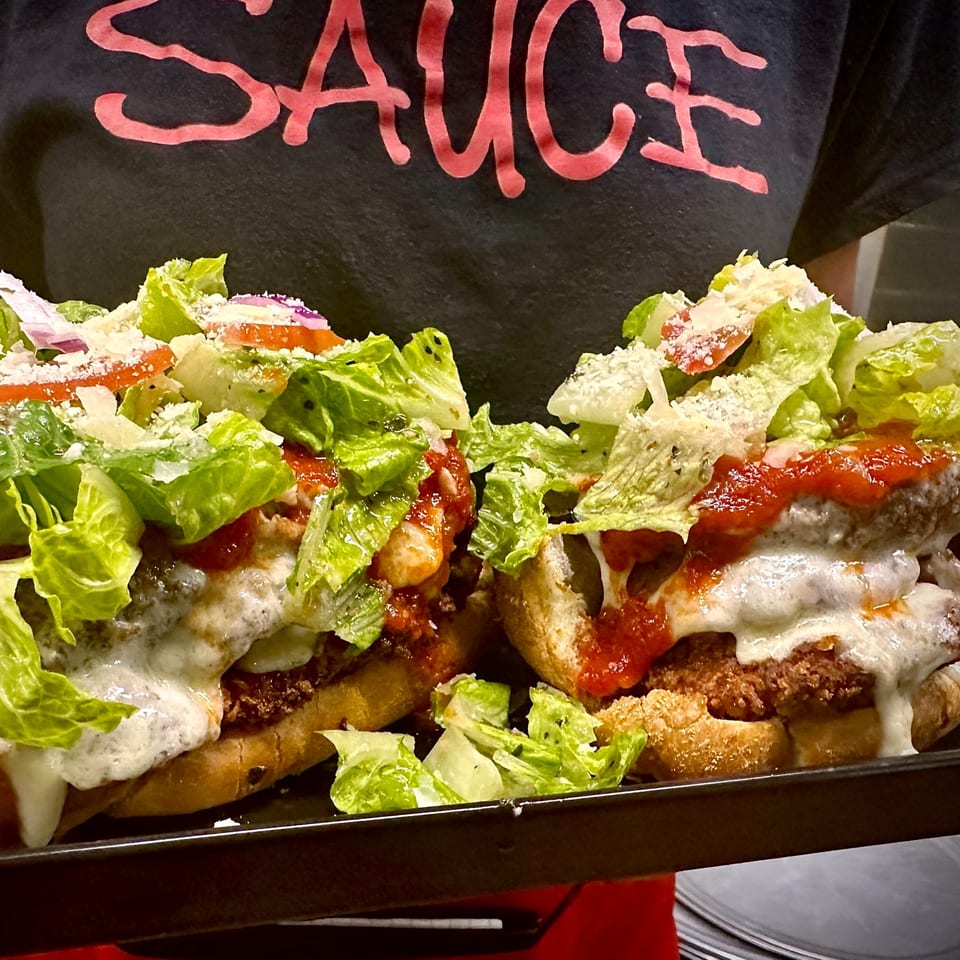 Two chicken parmesan subs with lettuce, tomato, and cheese on a black tray.