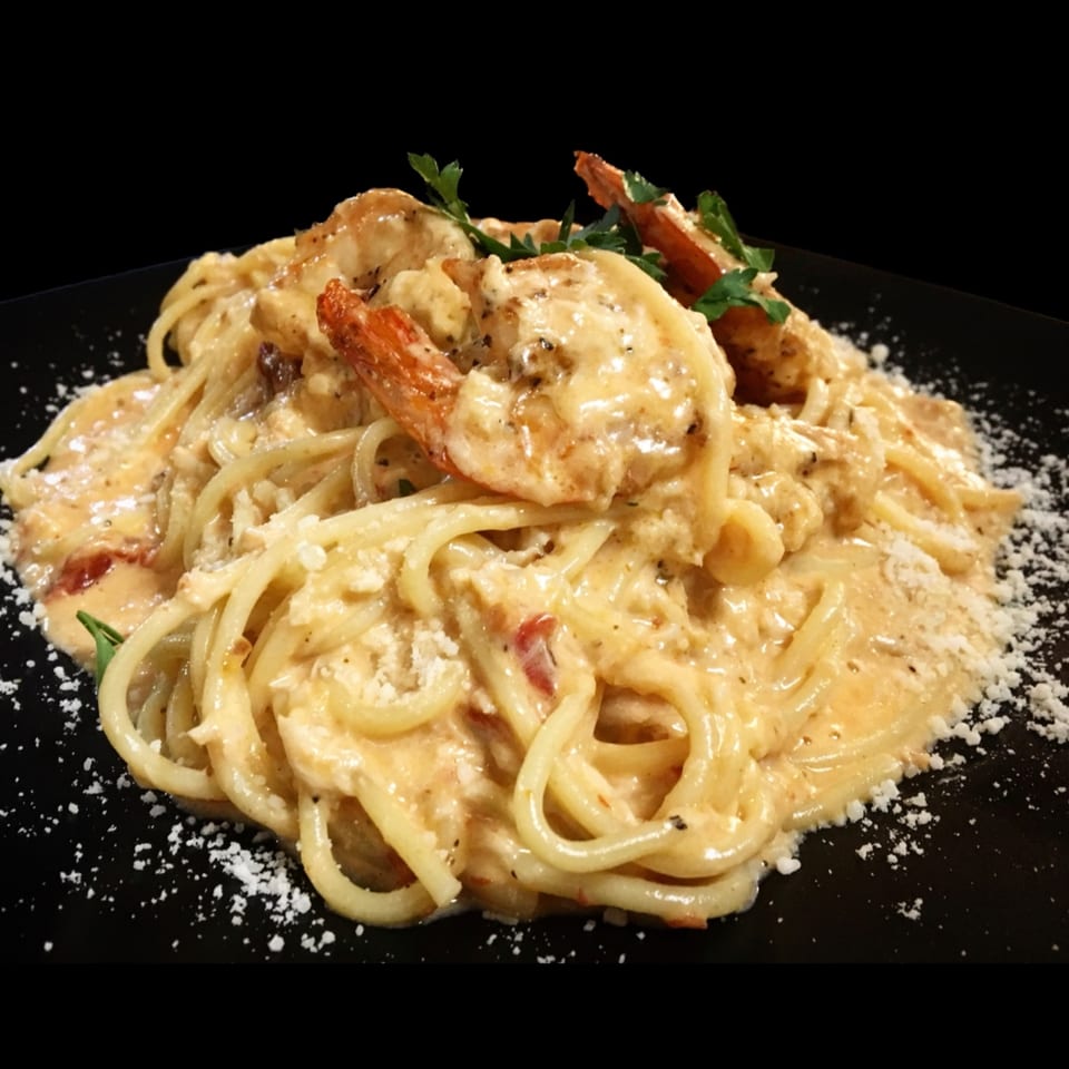 Creamy shrimp pasta with spaghetti, garnished with parsley and grated cheese on a black plate.