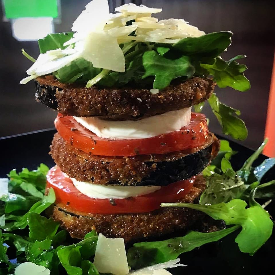 Stacked fried eggplant, mozzarella, and tomato slices, topped with arugula and shaved Parmesan.