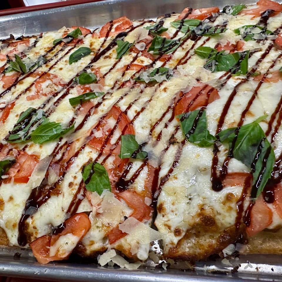 Sauce's rectangular pizza with melted mozzarella, sliced tomatoes, fresh basil, and balsamic glaze.