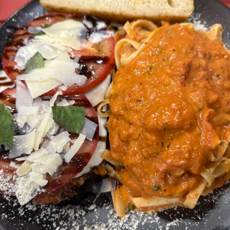 A plate of pasta with red sauce next to a Caprese salad with balsamic glaze and bread.
