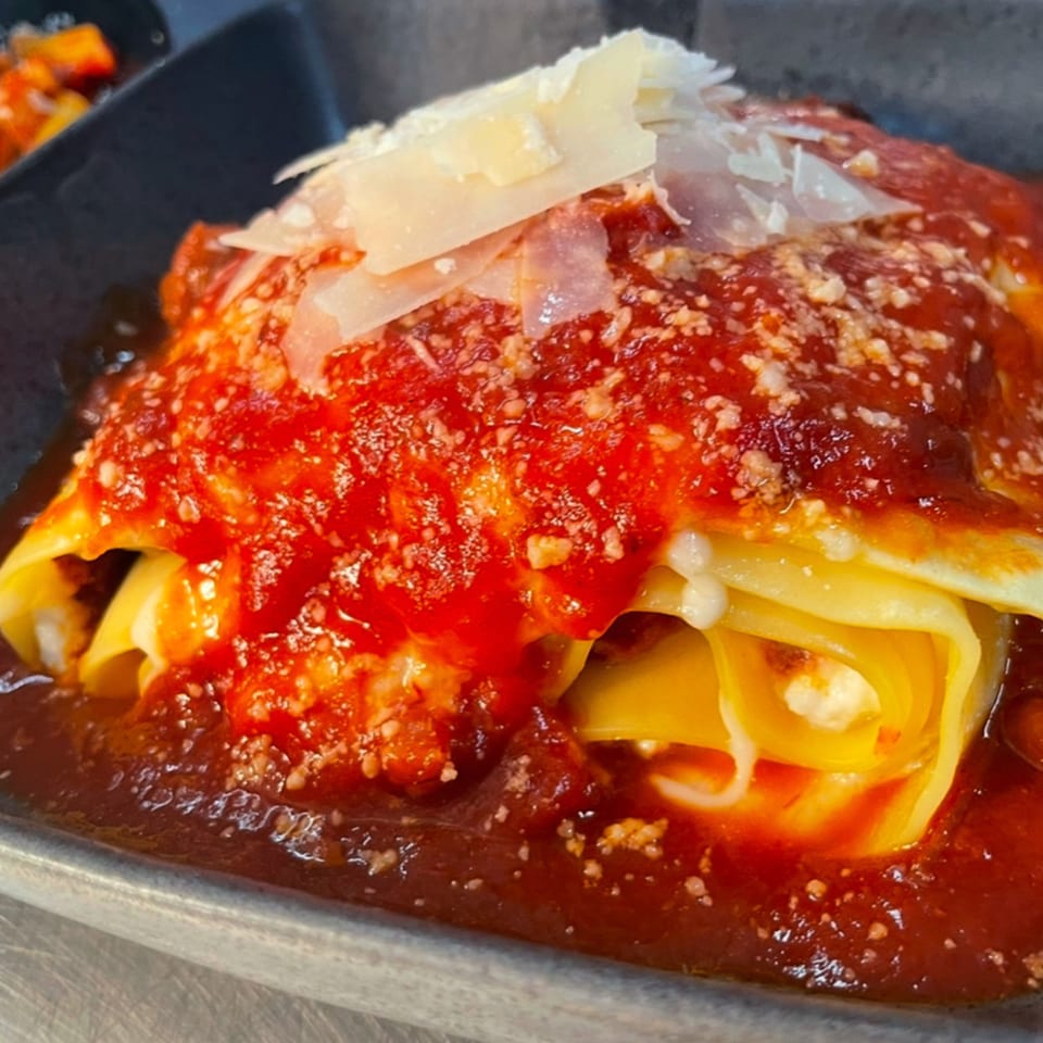 Close-up of lasagna with rich red sauce and shaved Parmesan cheese on top.