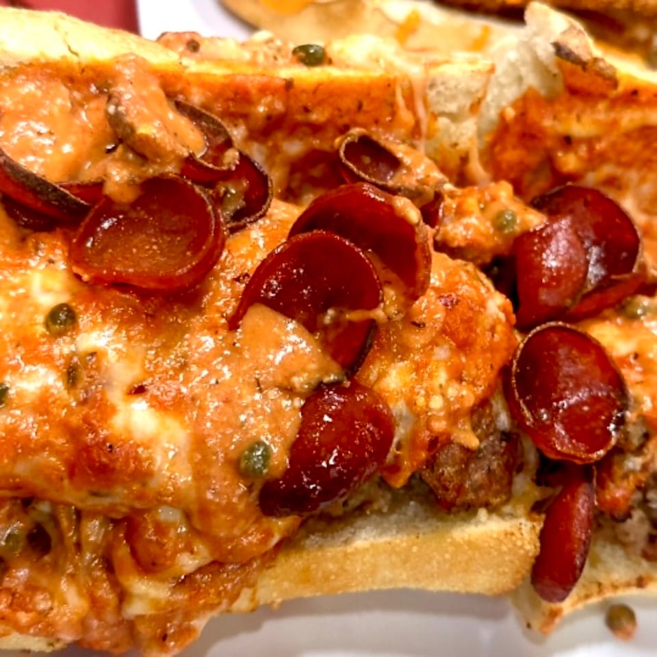 Close-up of a pizza sub with melted cheese, pepperoni, and sauce on a toasted bun.