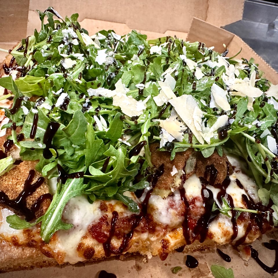 Sauce's pizza with arugula, parmesan, and balsamic glaze in a cardboard box.