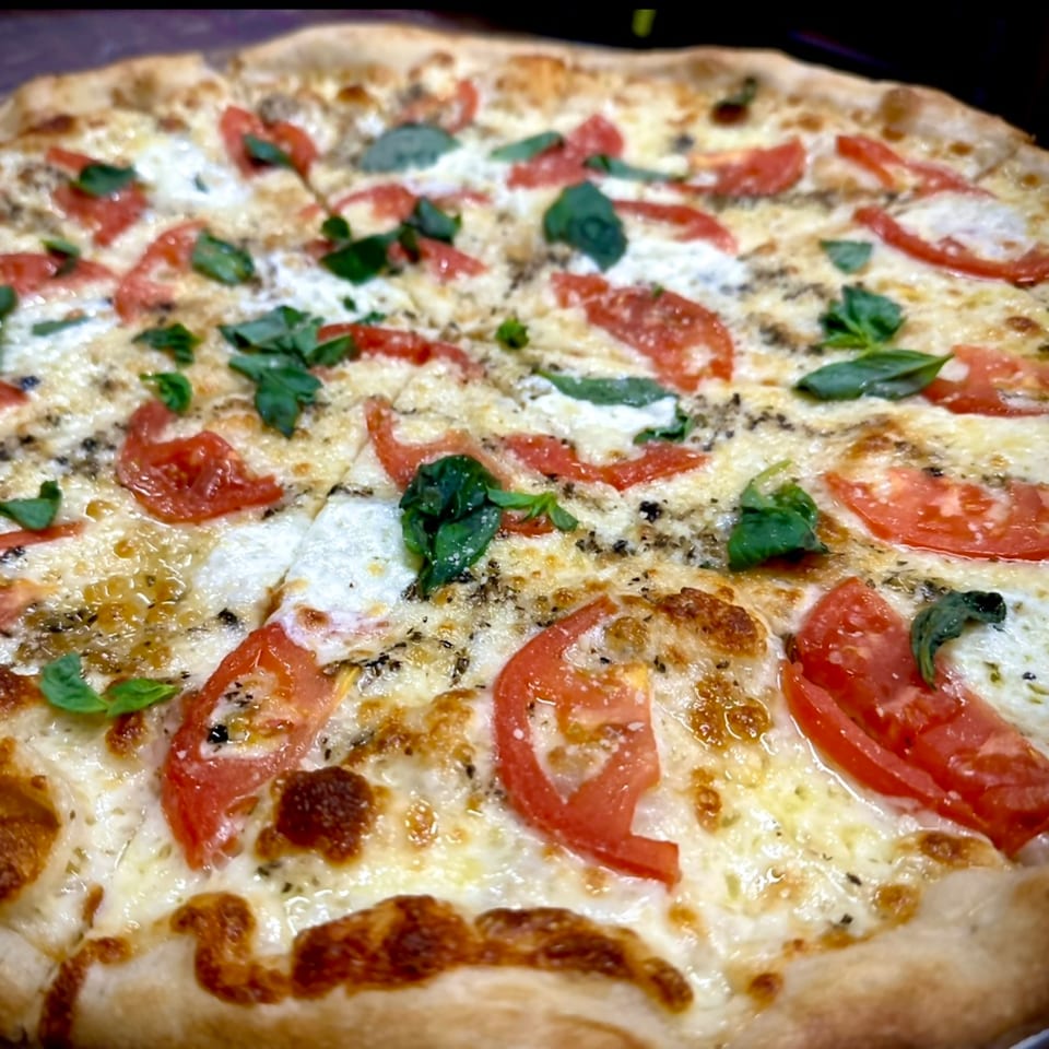 Close-up of a Sauce pizza with melted cheese, sliced tomatoes, and fresh basil leaves.