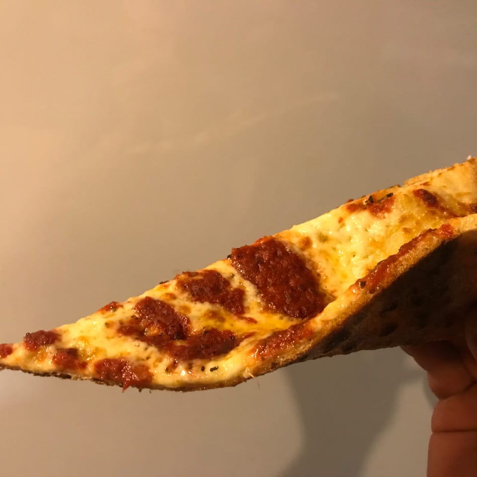 A hand holds up a slice of Sauce's pepperoni pizza, with melted cheese and red sauce.